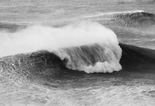 Eine Welle bricht am Strand in Schwarz und Weiß