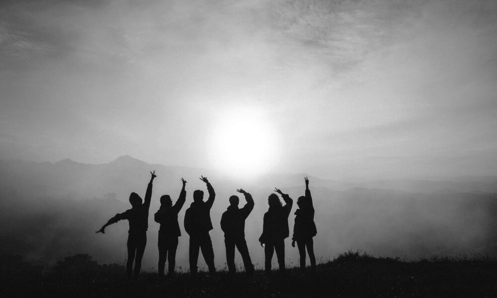Eine Gruppe Menschen steht mit dem Rücken vor einem Sonnenaufgang