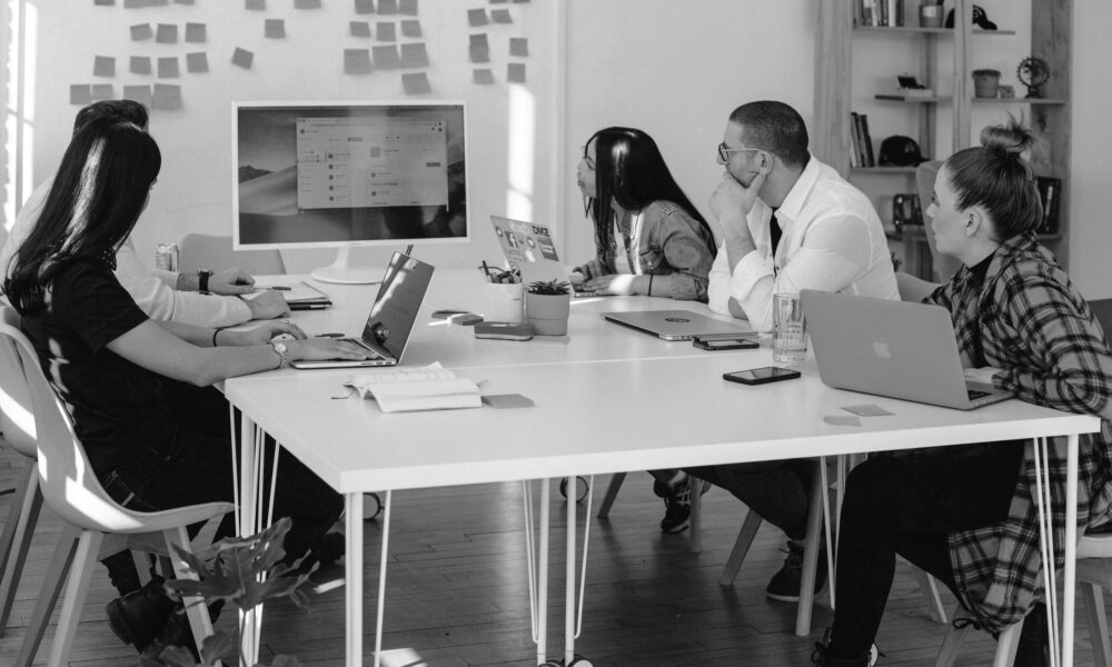 Personen sitzen gemeinsam am Tisch und schauen auf einen Bildschirm