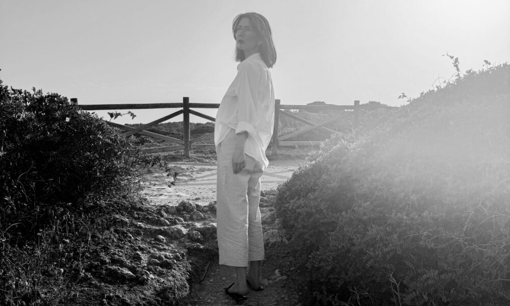 Eine Frau steht auf einem Weg und hat den Blick in die Ferne gewandt